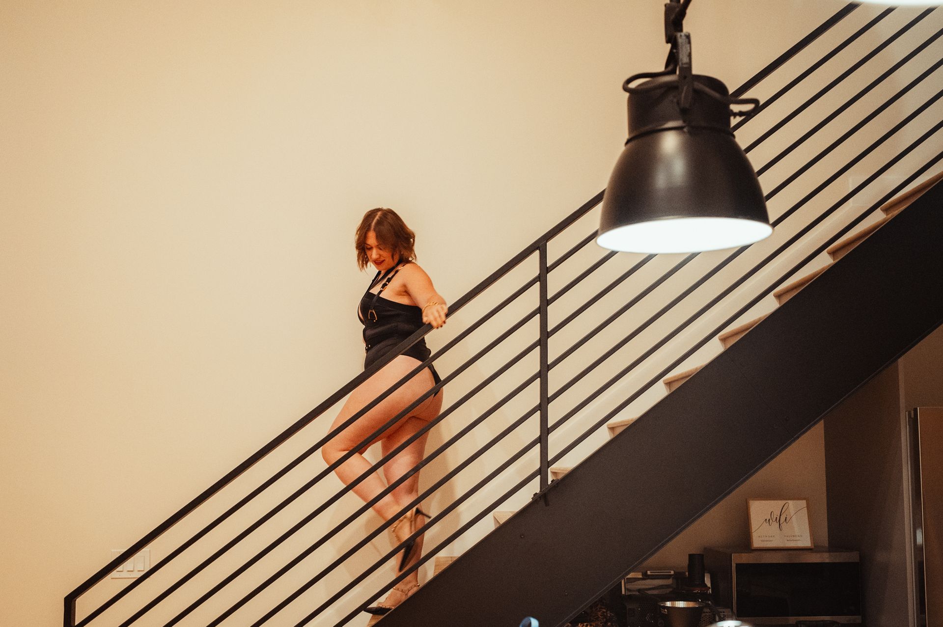 A woman in a black swimsuit stands confidently on the stairs, showcasing her poised demeanor and stylish swimwear.