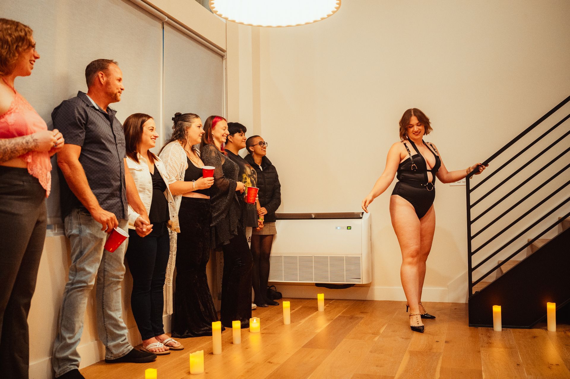 A woman in a black bodysuit poses confidently on a polished wooden floor, showcasing elegance and strength.