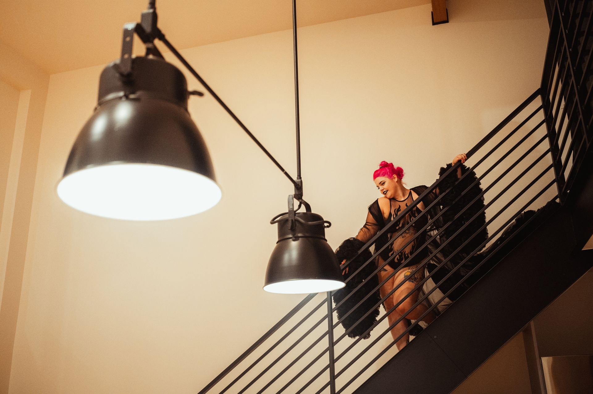 A woman with pink hair wearing a black dress stands gracefully on a staircase, exuding elegance and style.