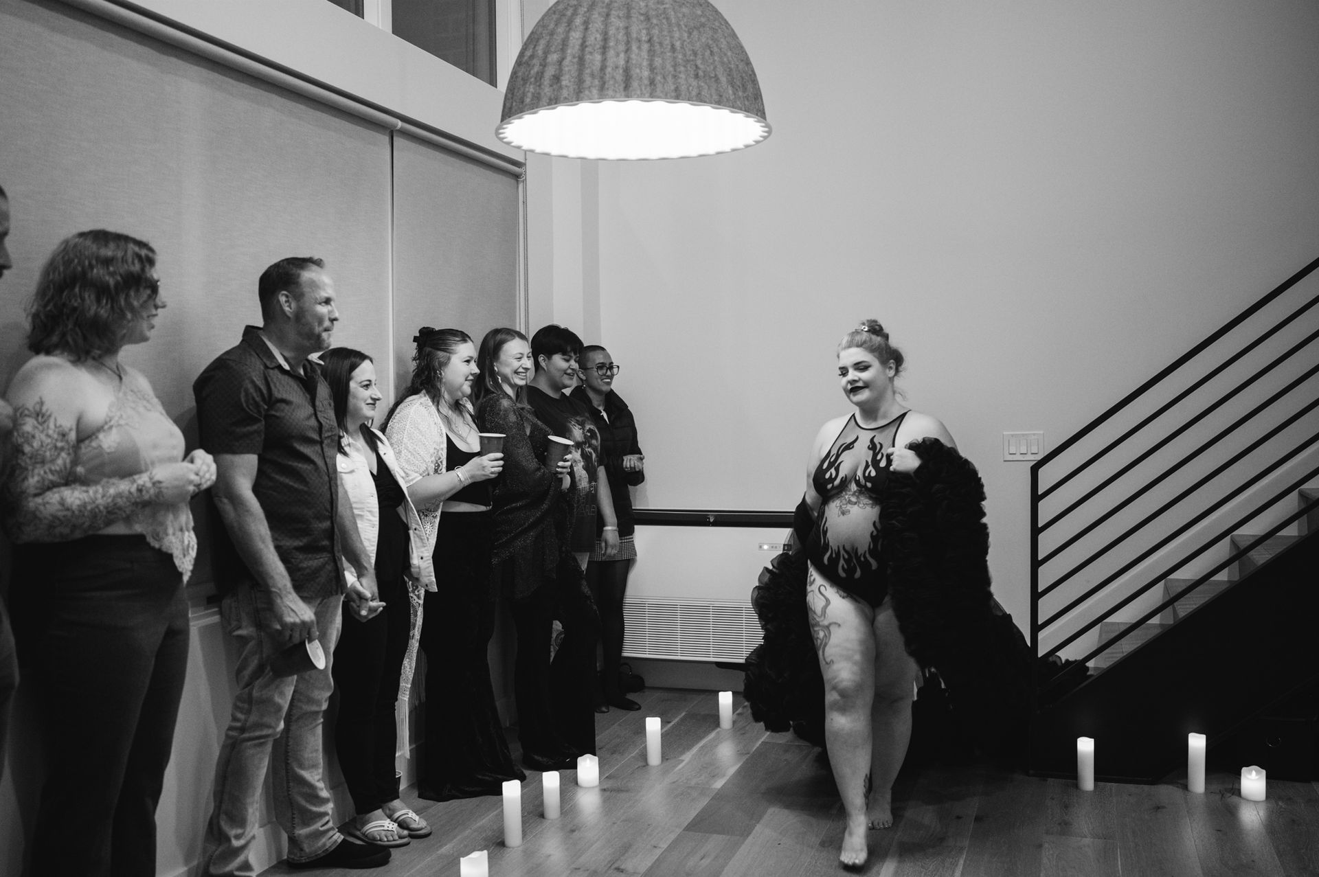 A woman in a black dress stands confidently before a gathering of people, engaging their attention and interest.