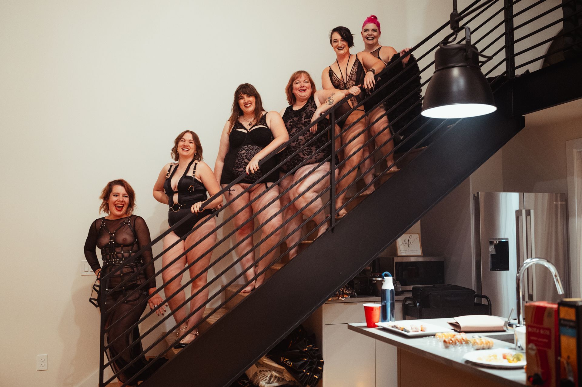 A group of women in elegant lingerie poses confidently on a stylish staircase, showcasing beauty and camaraderie.