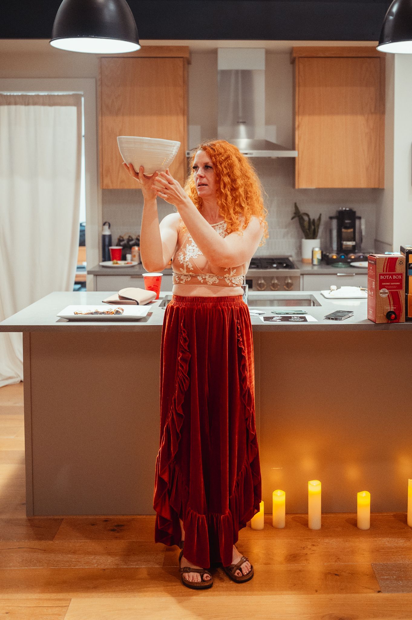 A woman with vibrant red hair holds a bowl in her hands.