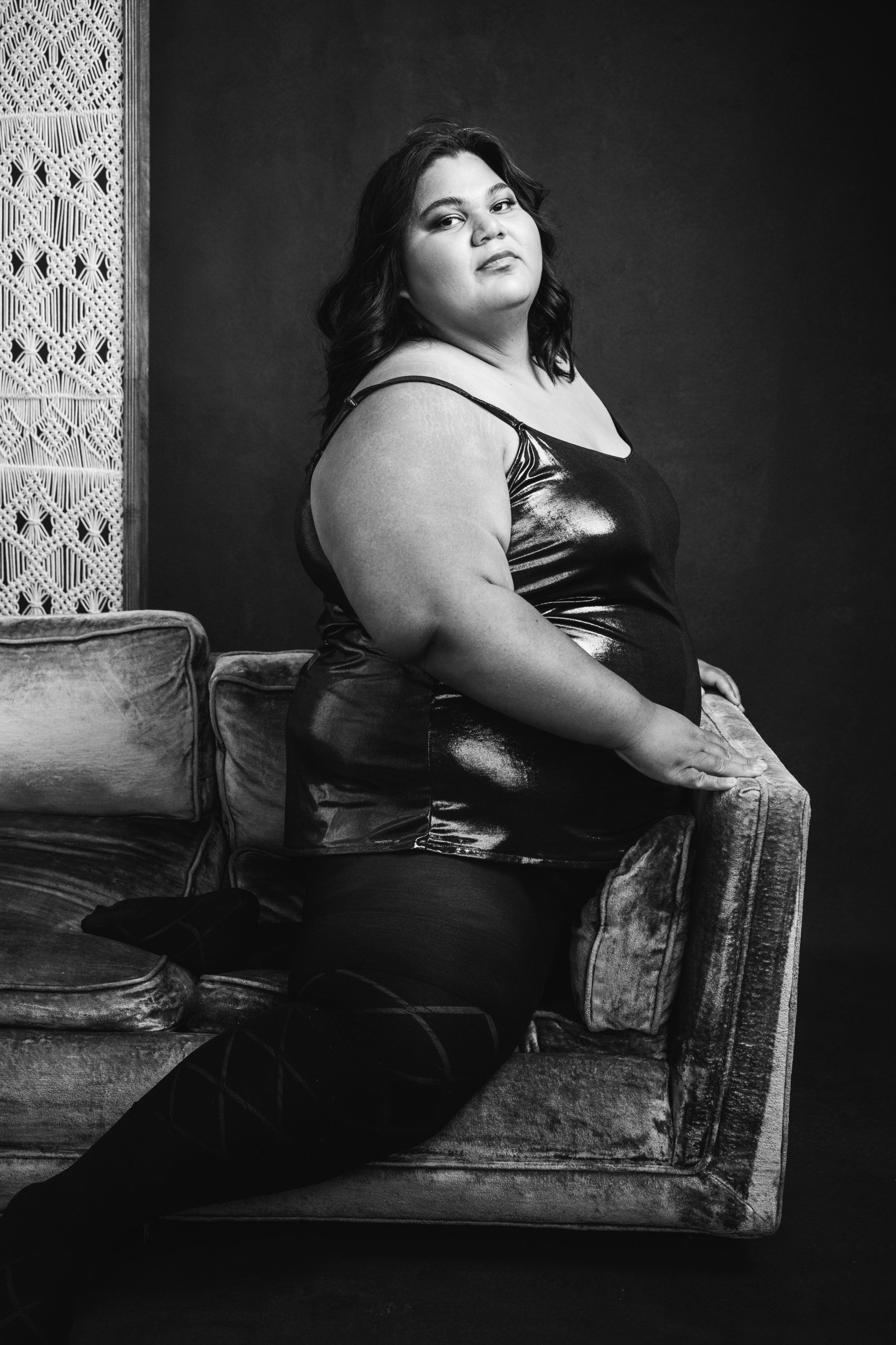 A woman posing on a couch in front of a wall.