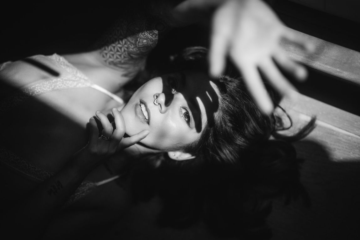 A woman lies on the floor with her arms raised above her head, expressing a moment of relaxation or surrender.