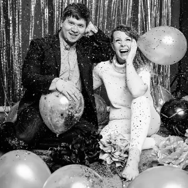 A pair enjoying a festive moment on the floor with confetti and balloons.