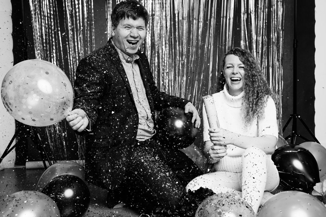 A pair enjoying a festive moment on the floor with confetti and balloons.