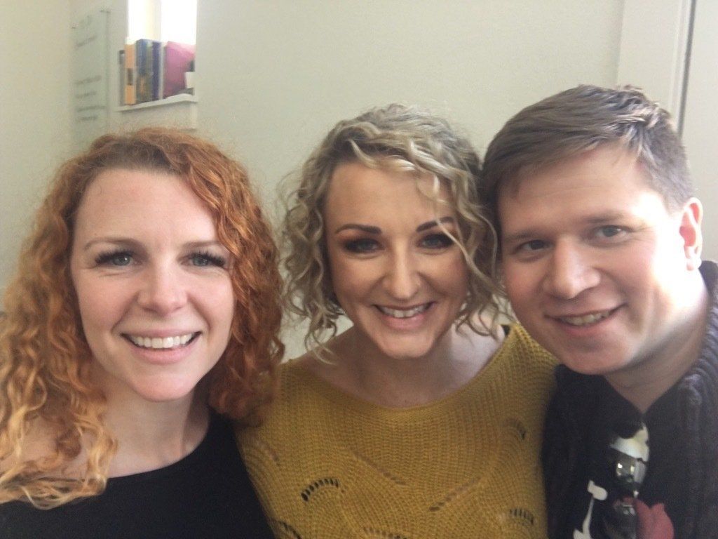 Three people smiling, posing for a photo in a room.