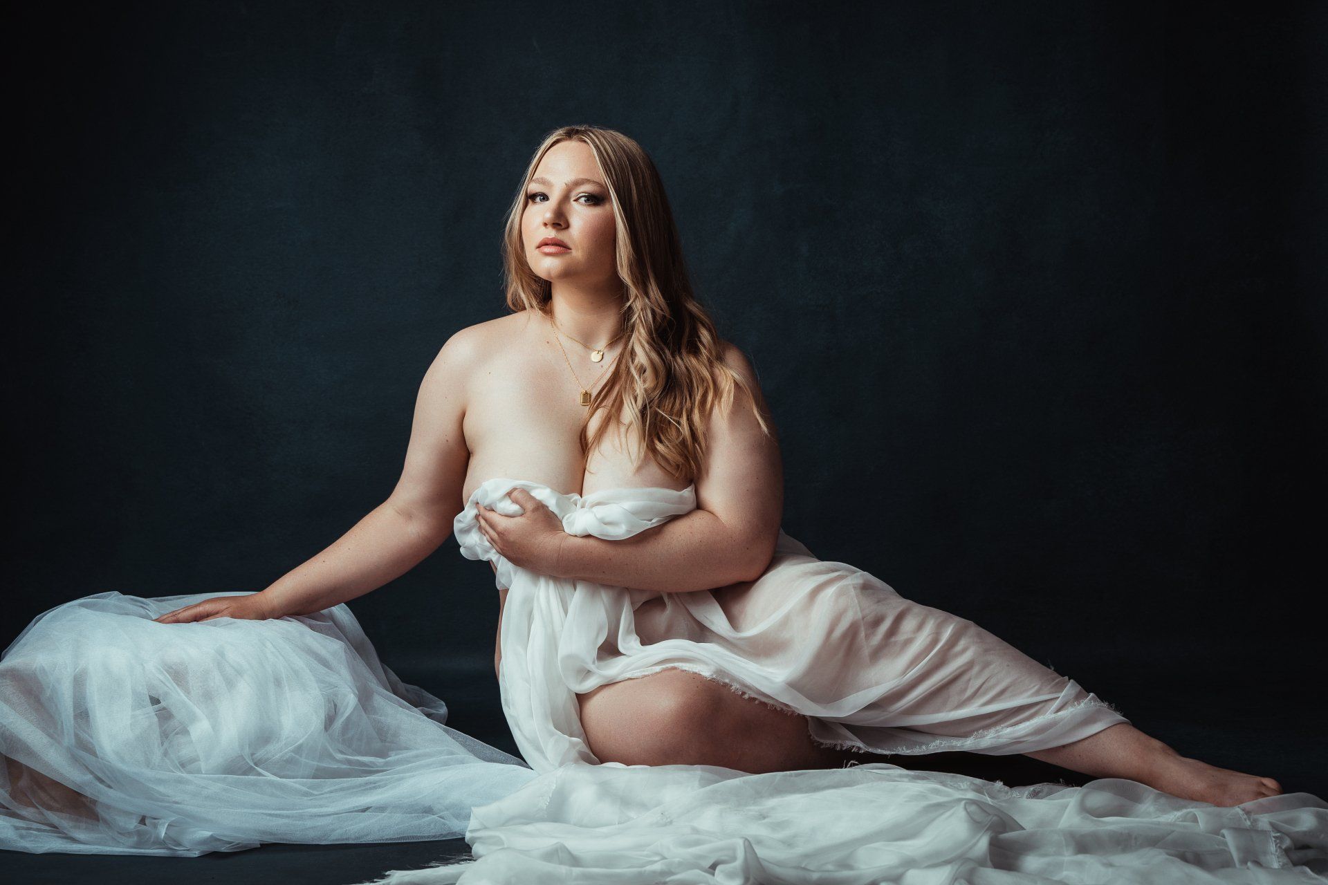 A nude woman in a white dress sitting on a black background.