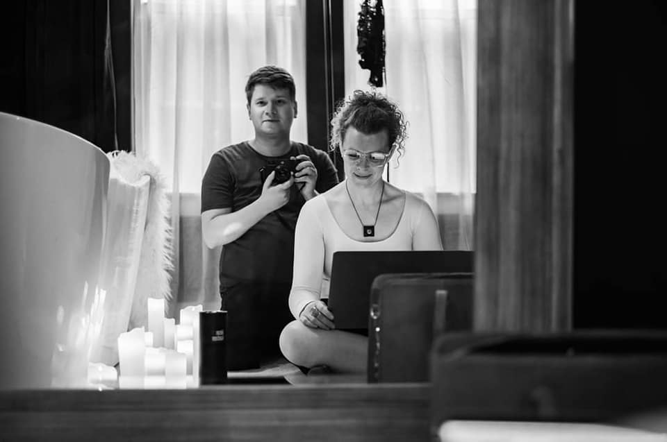 A man and woman sitting together with a laptop in a bathroom.