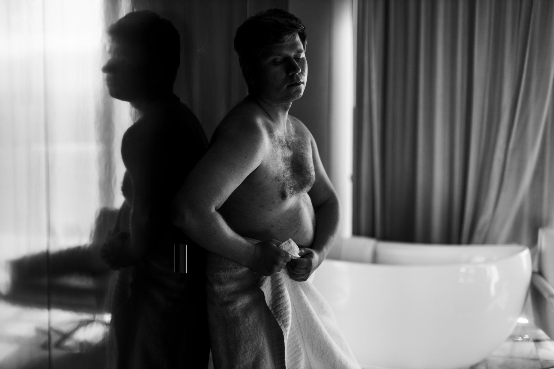 man standing next to a bathtub wrapped in a towel during his boudoir session