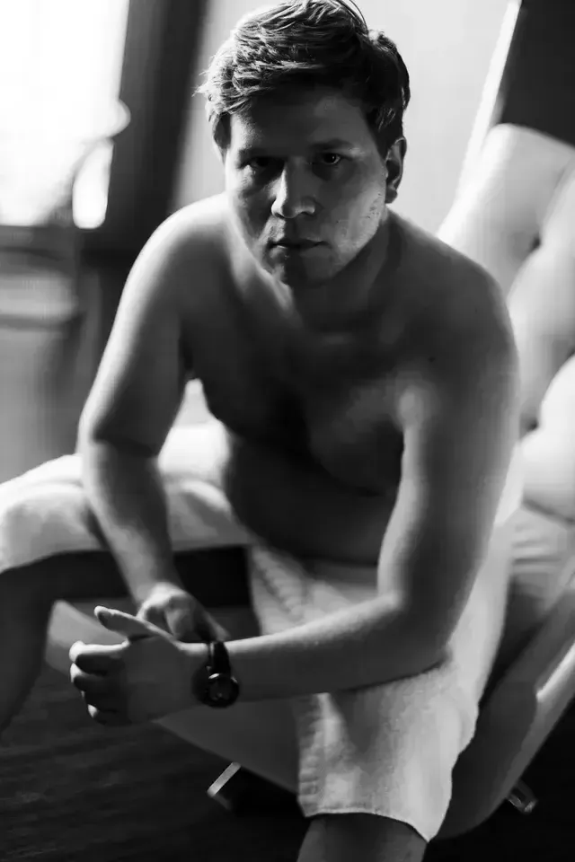 male sitting down with a towel wrapped around him fixing his watch during the boudoir session