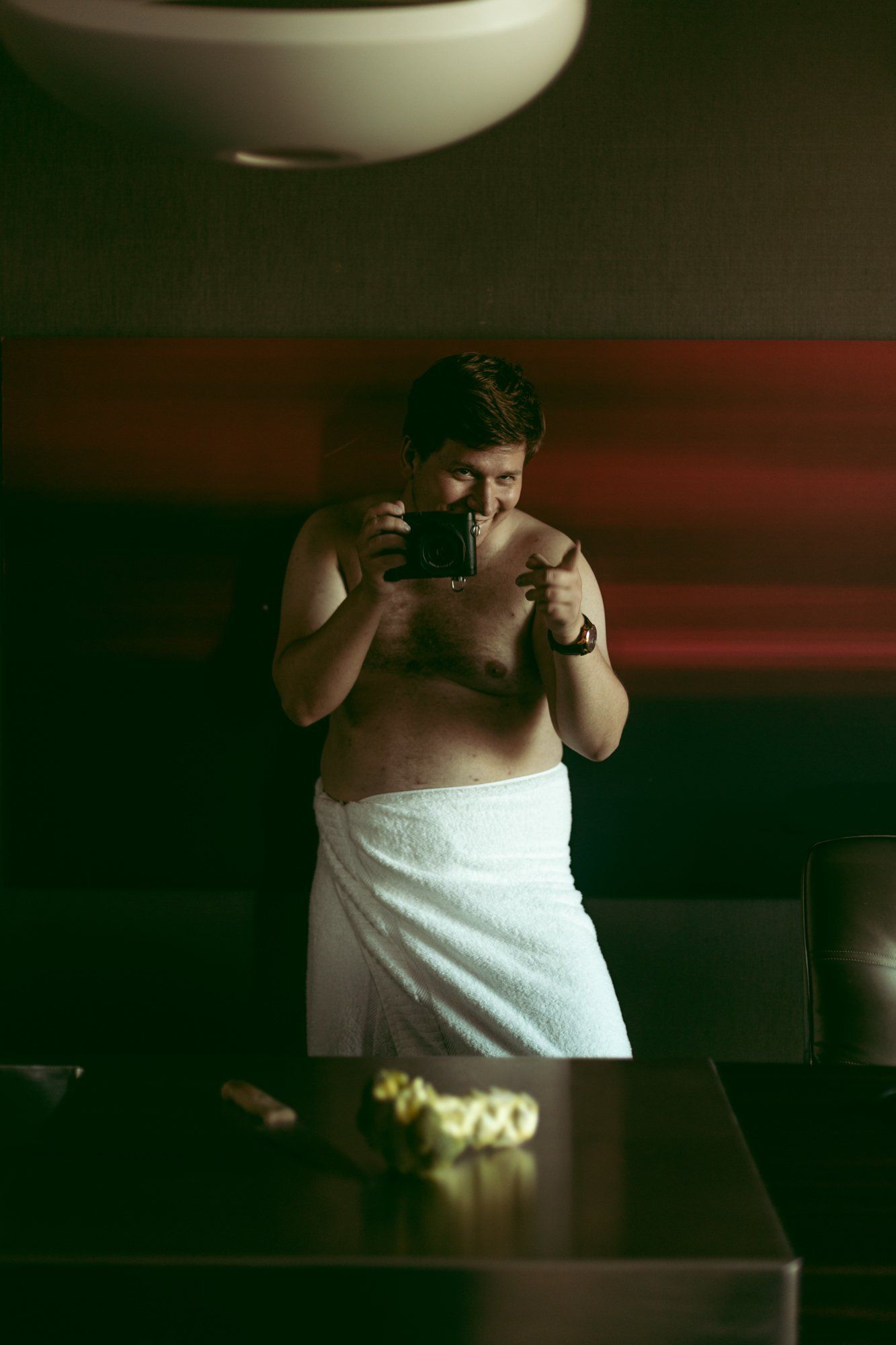 man standing and laughing wrapped in a towel while holding a camera during his boudoir photo session