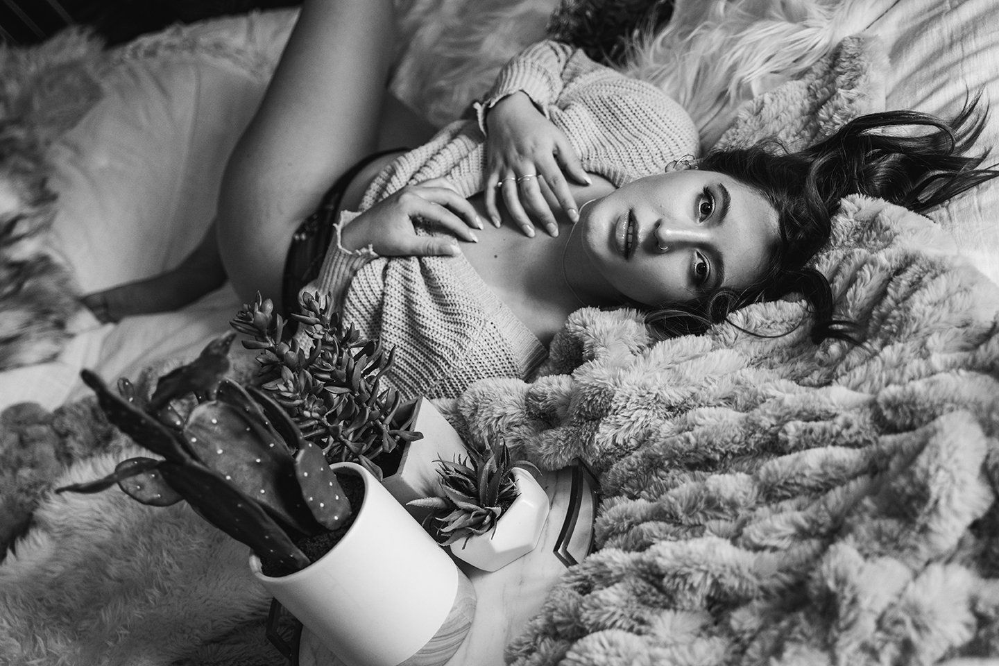 Best Boudoir Utah young woman laying on bed on her back wearing a sweater and looking at the camera during boudoir session