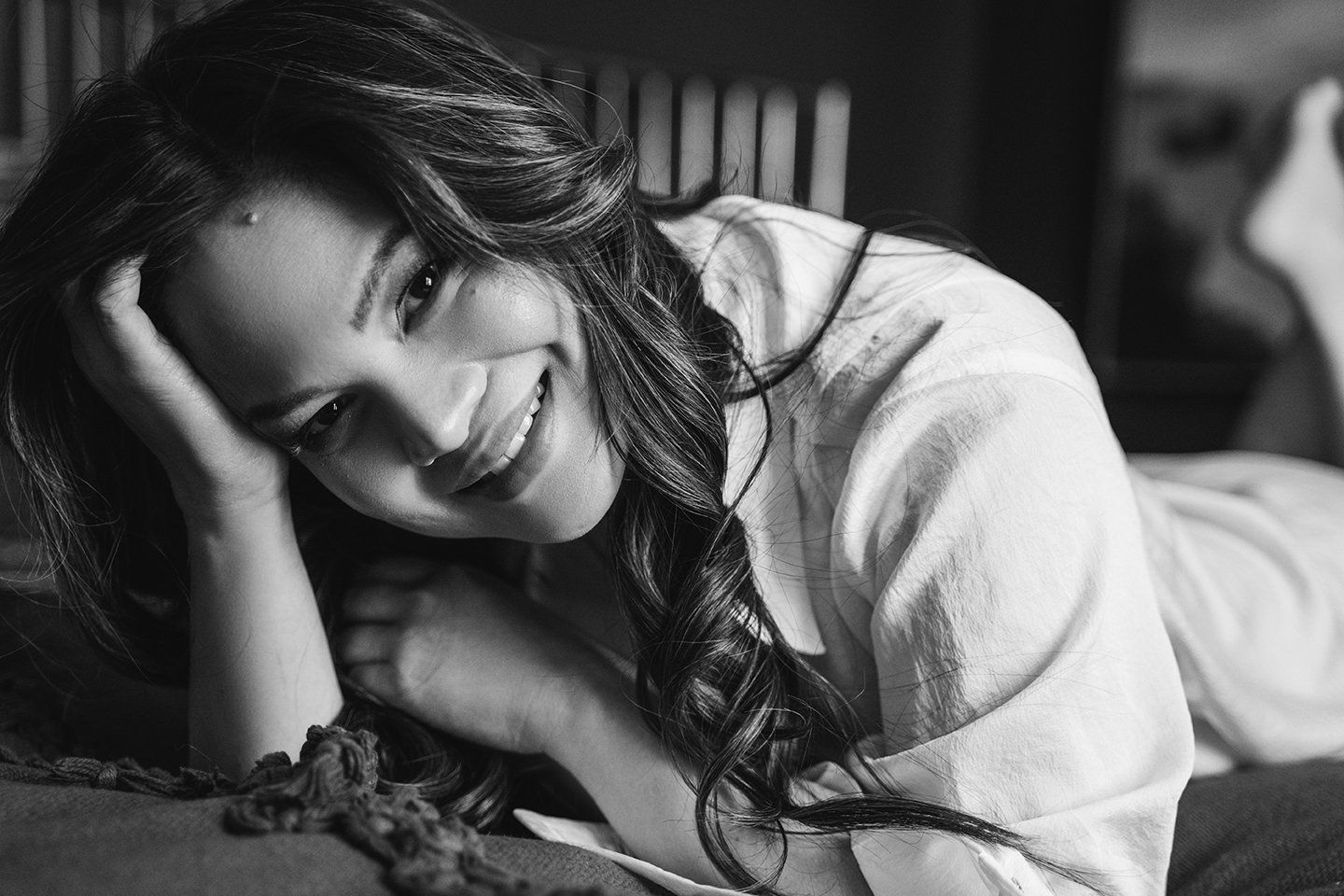Award Winning Boudoir Studio in Utah woman laying on the bed in button up shirt and smiling at the camera