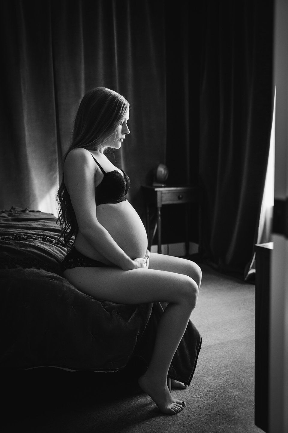 pregnancy boudoir shoot woman sitting on bed with hands on belly