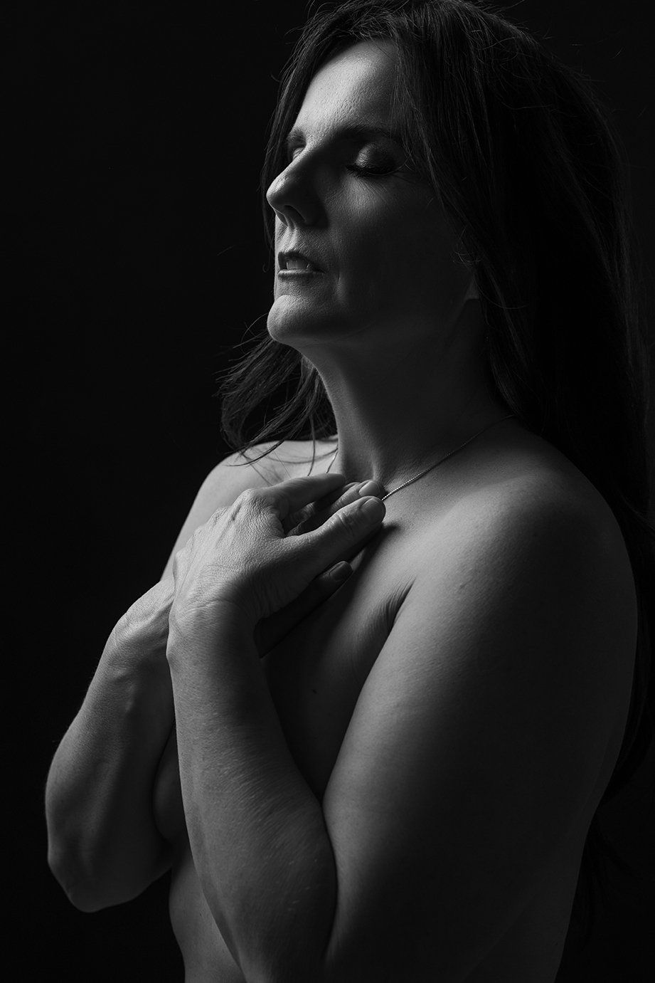 nude portrait of a woman with eyes closed, hands on collar bones