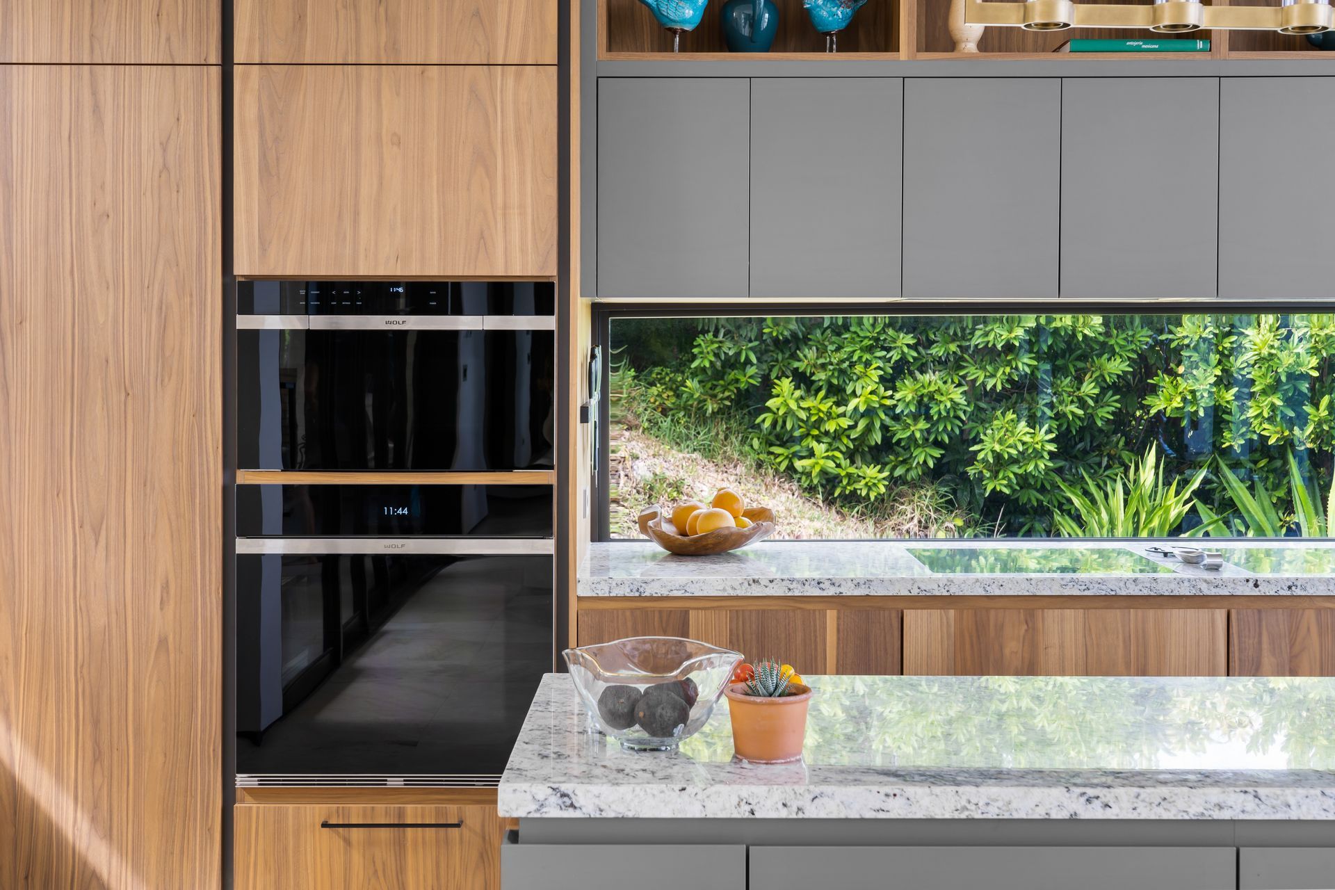 A kitchen with wooden cabinets , gray counter tops , and a window.