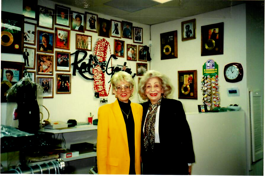 Two women are posing for a picture in front of a wall that has pictures on it
