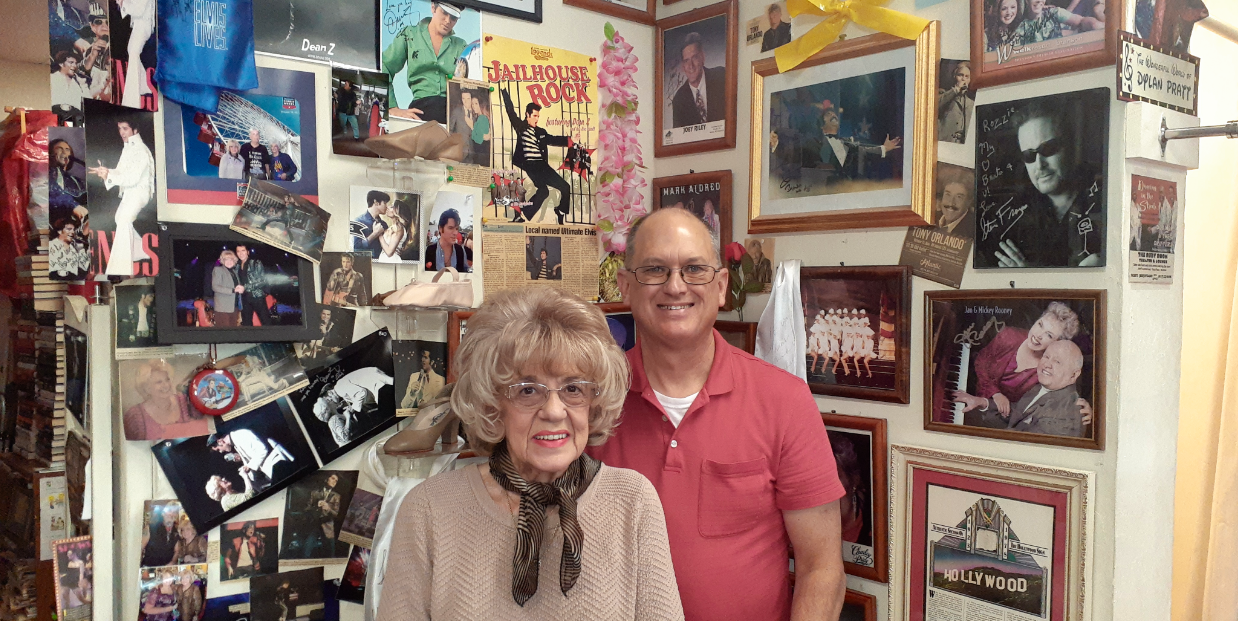 A man and a woman are standing in front of a wall covered in pictures.