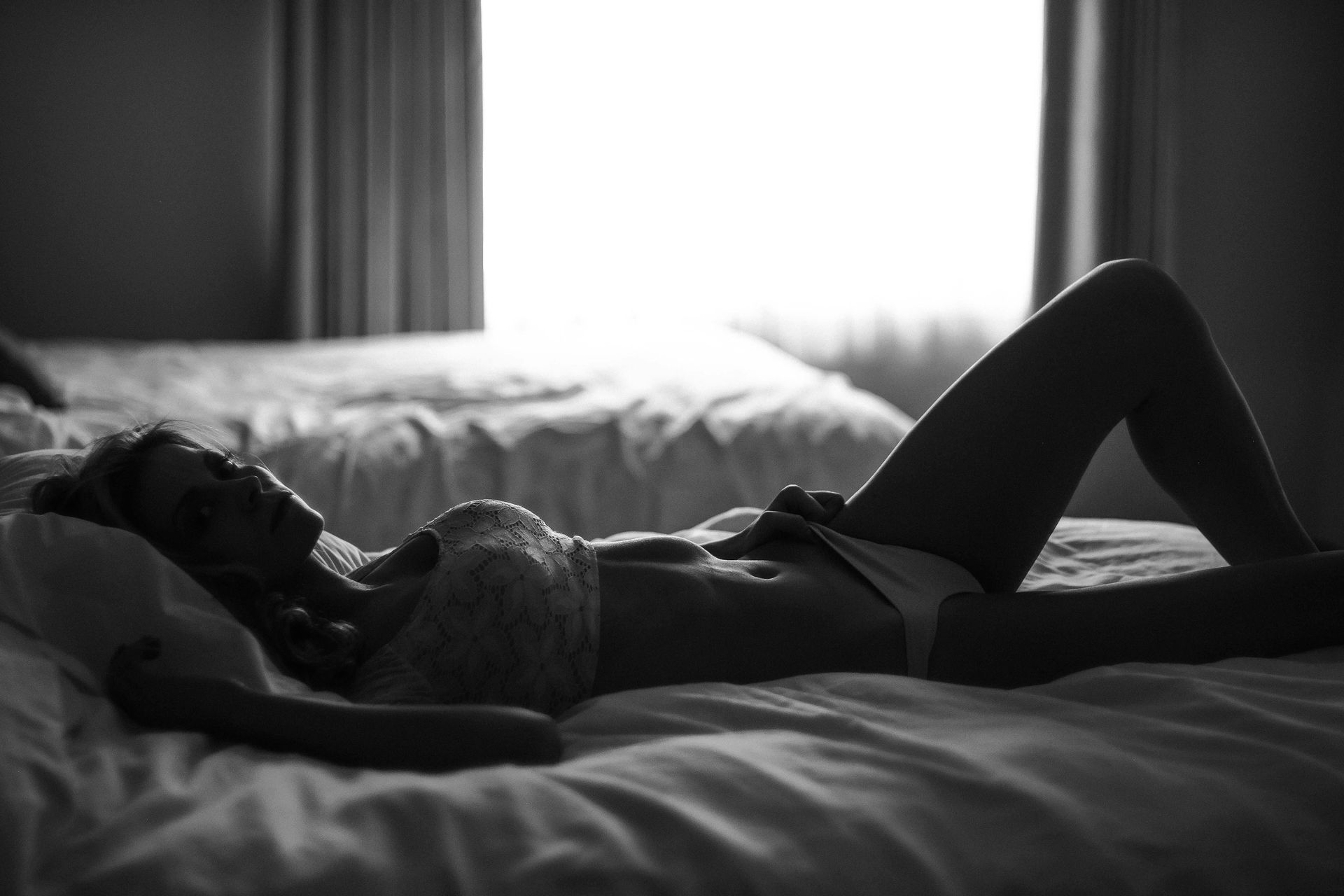 A woman in lingerie is laying on a bed in a black and white photo.