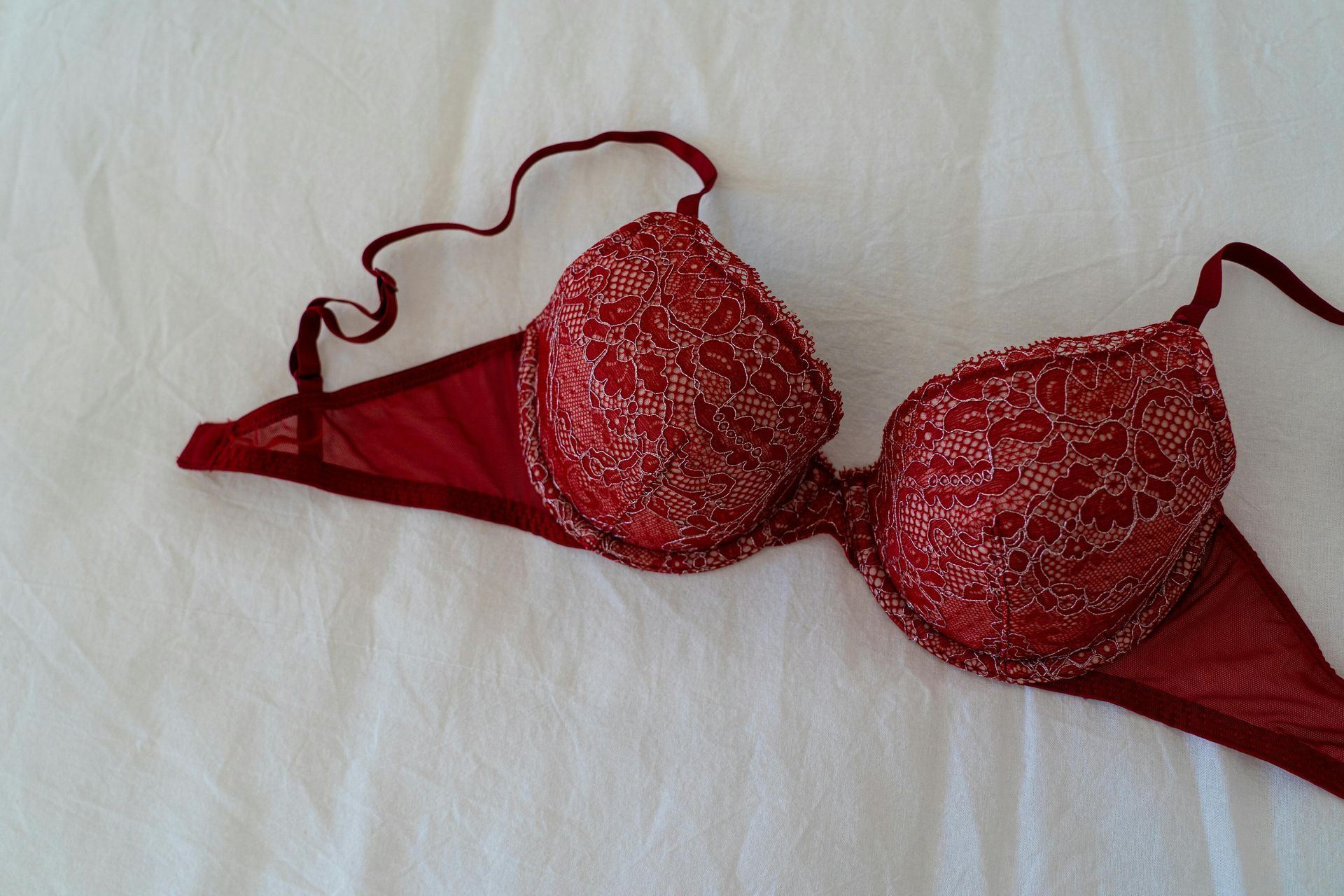 A red bra is laying on a white cloth