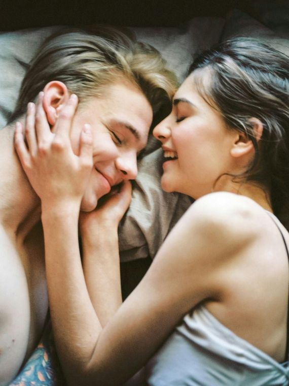 A man and a woman are laying in bed looking at each other and smiling.