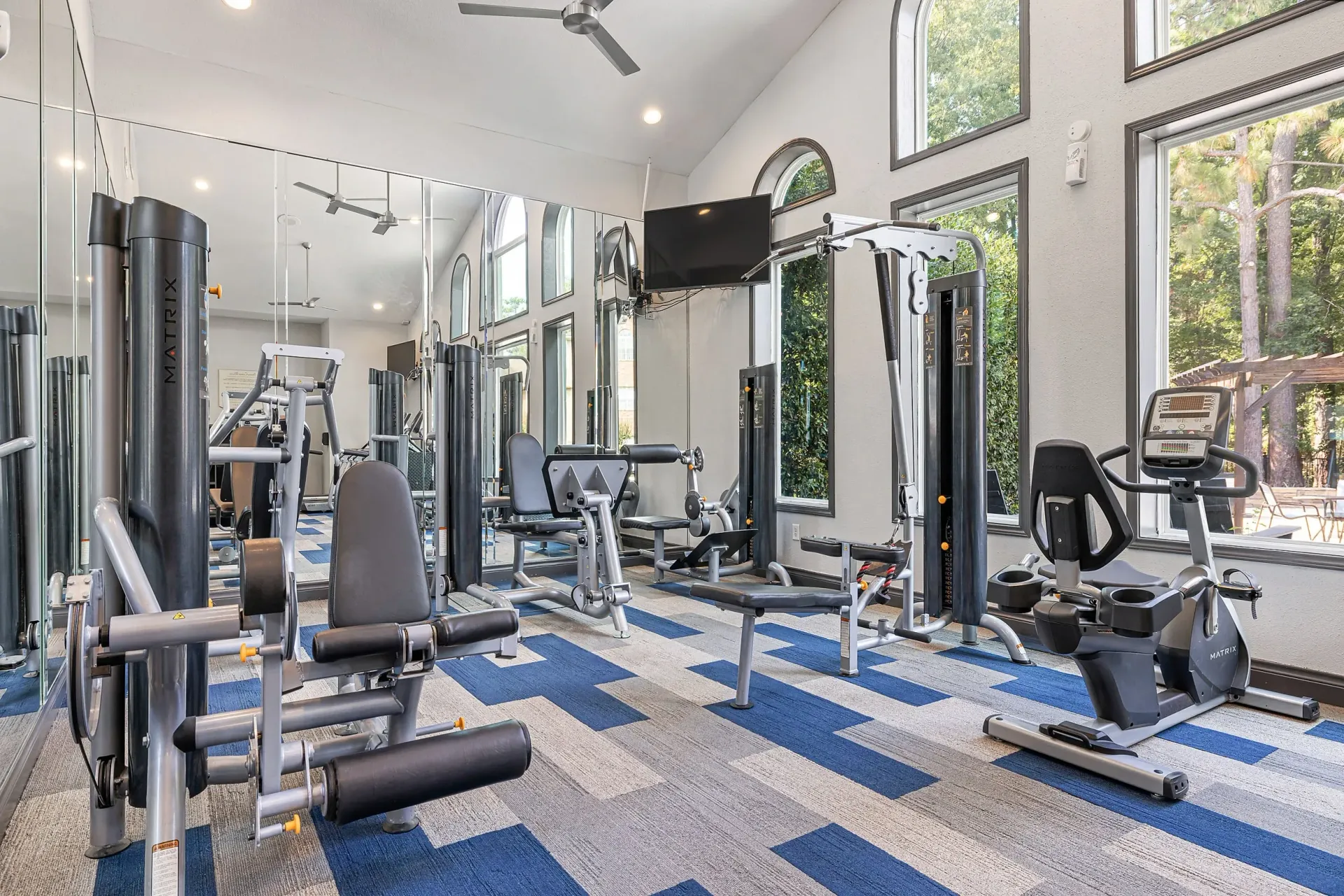 Fitness center with cardio and weight machines, large mirrors, and high ceilings.