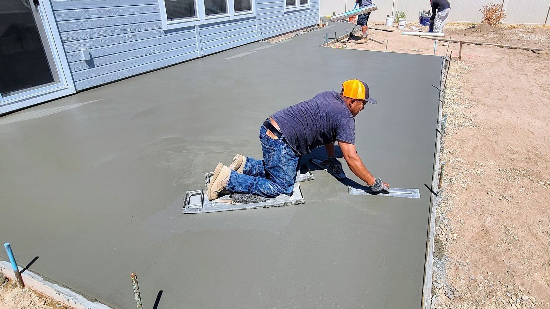 Crew member finishing a large freshly poured concrete patio slab using kneeboards and hand trowels n