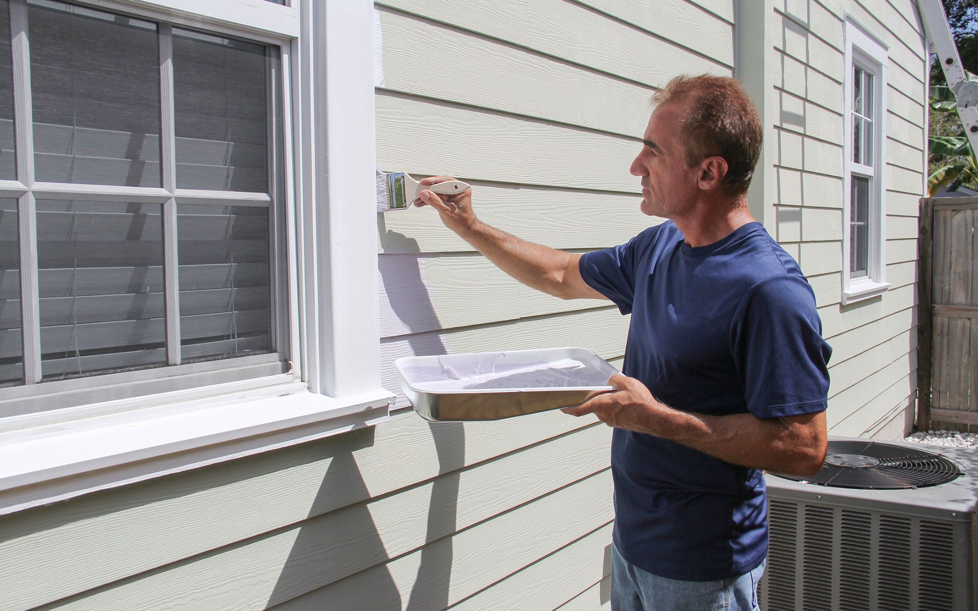A man is painting the side of a house with a brush.