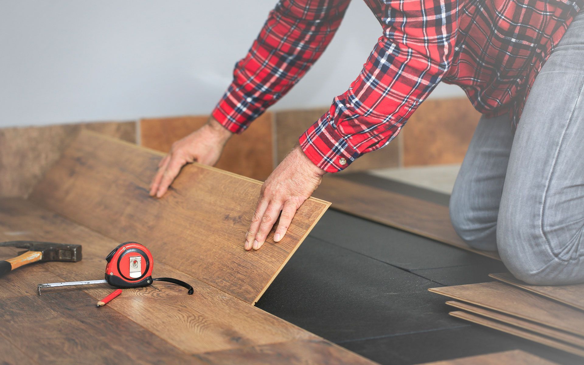 A man in a plaid shirt is installing a wooden floor.