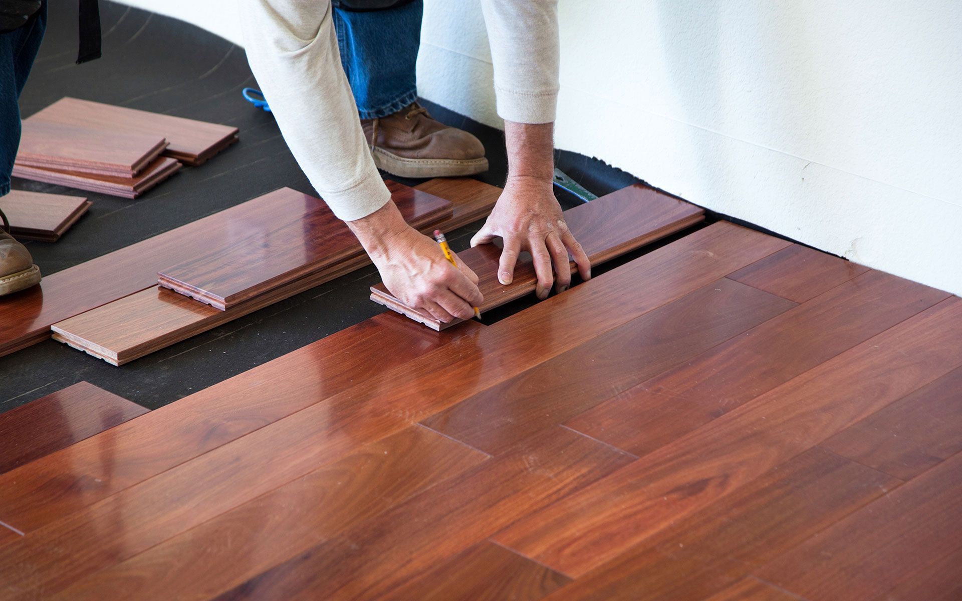 A person is measuring a piece of wood on a hardwood floor.