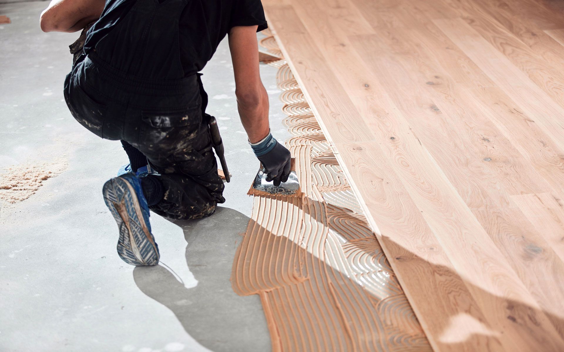 A man is applying glue to a wooden floor.