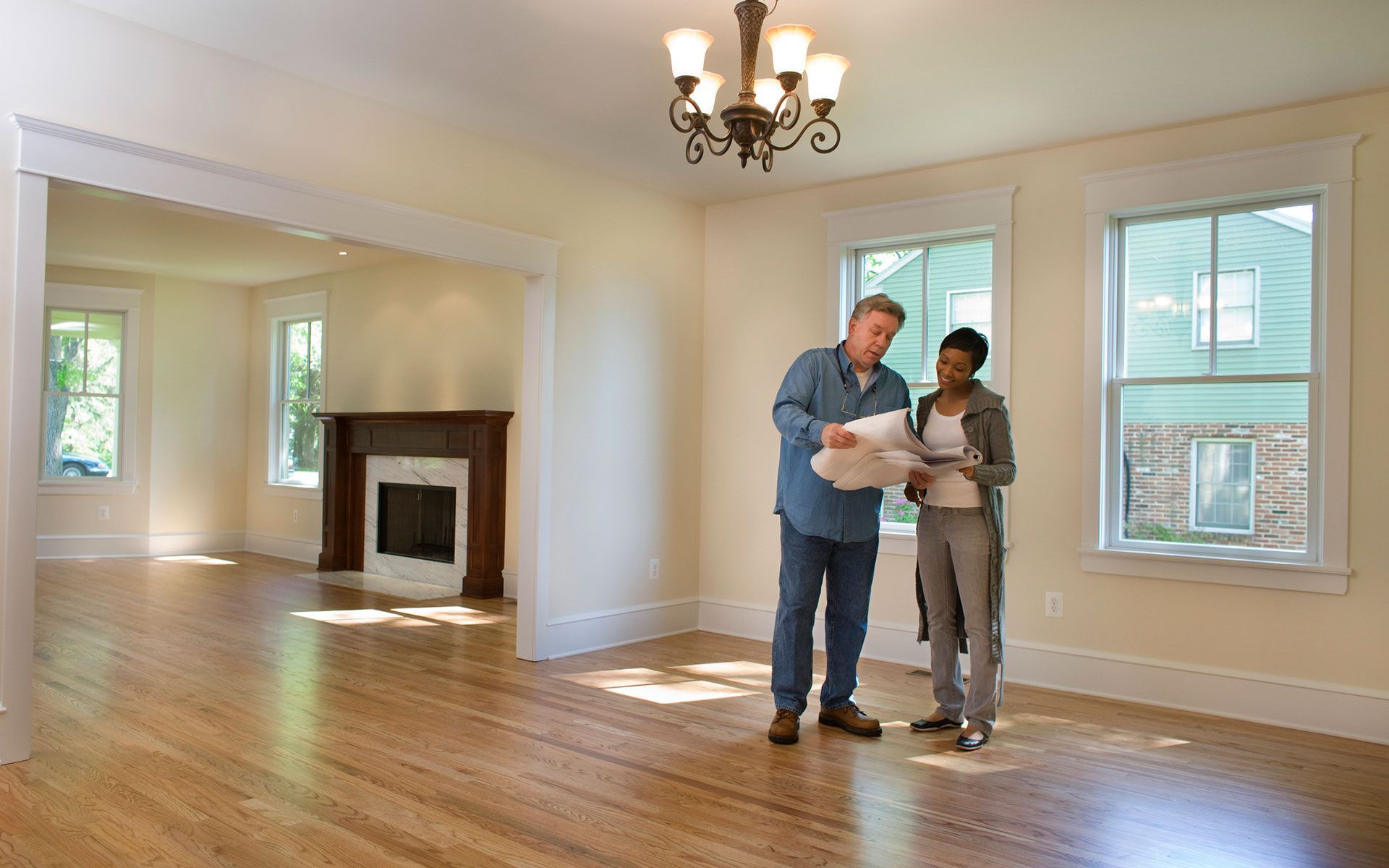 A man and a woman are standing in an empty room looking at a blueprint.