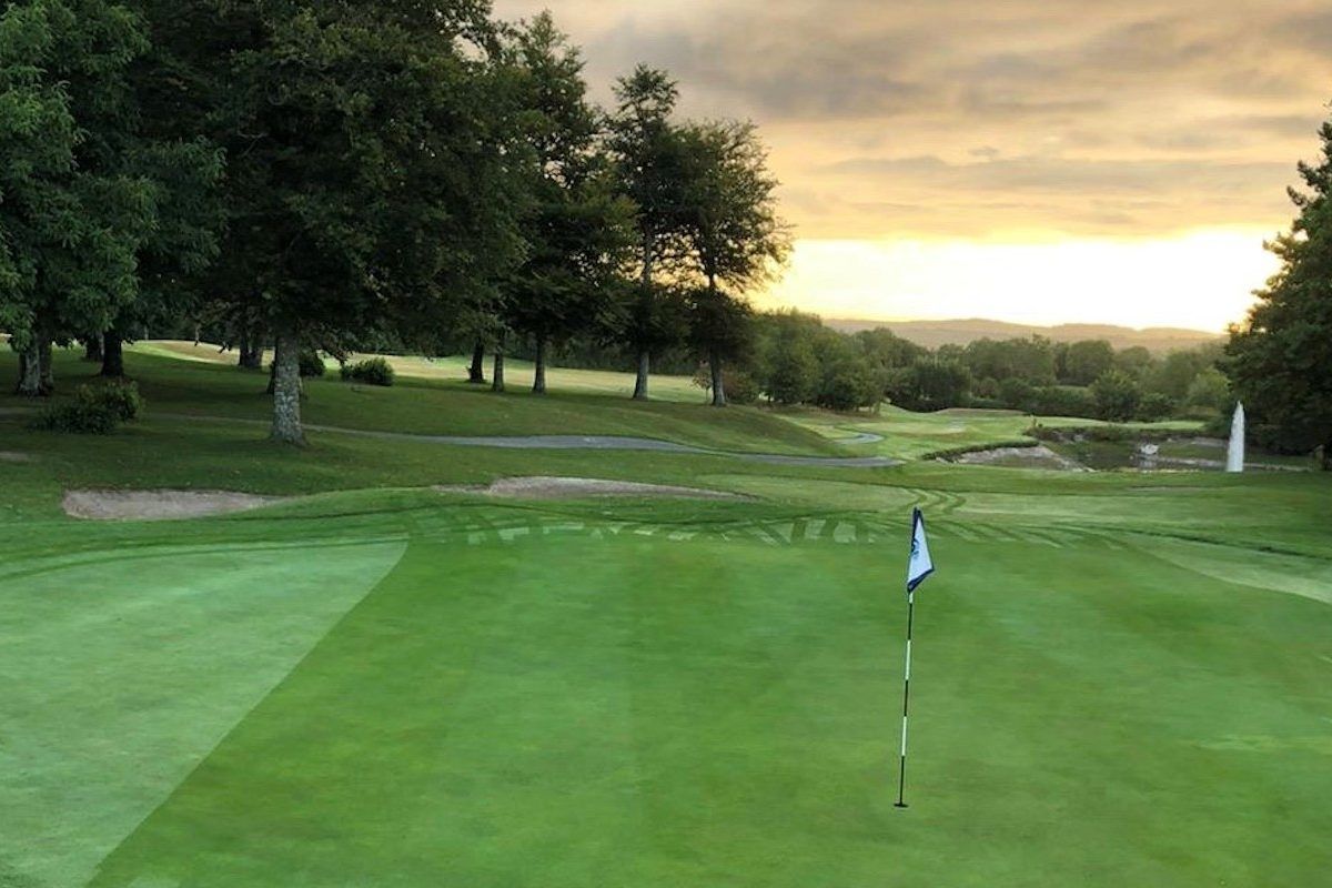 A golf course with a flag on the green at sunset.