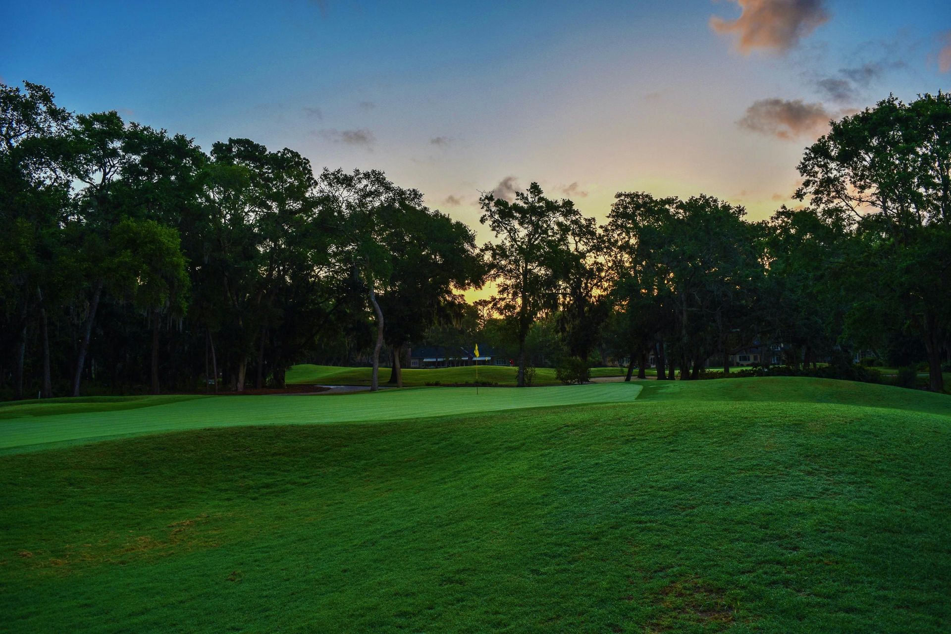 A golf course with trees in the background at sunset