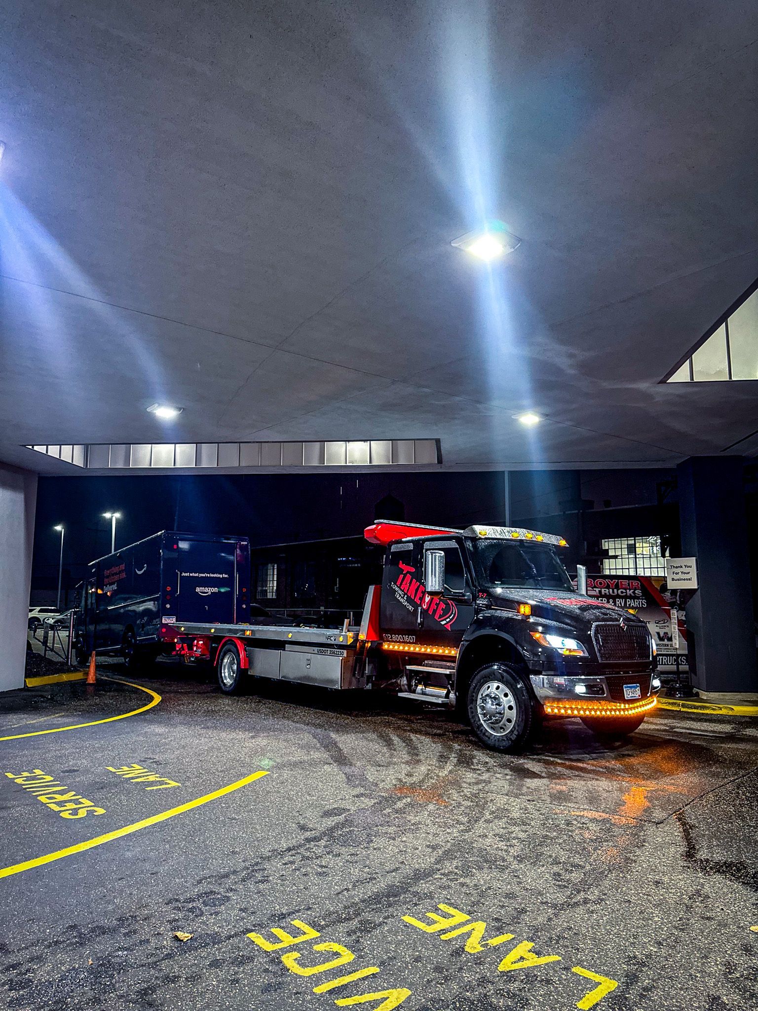 Tow truck with a vehicle, parked under a bridge with signage, at night.
