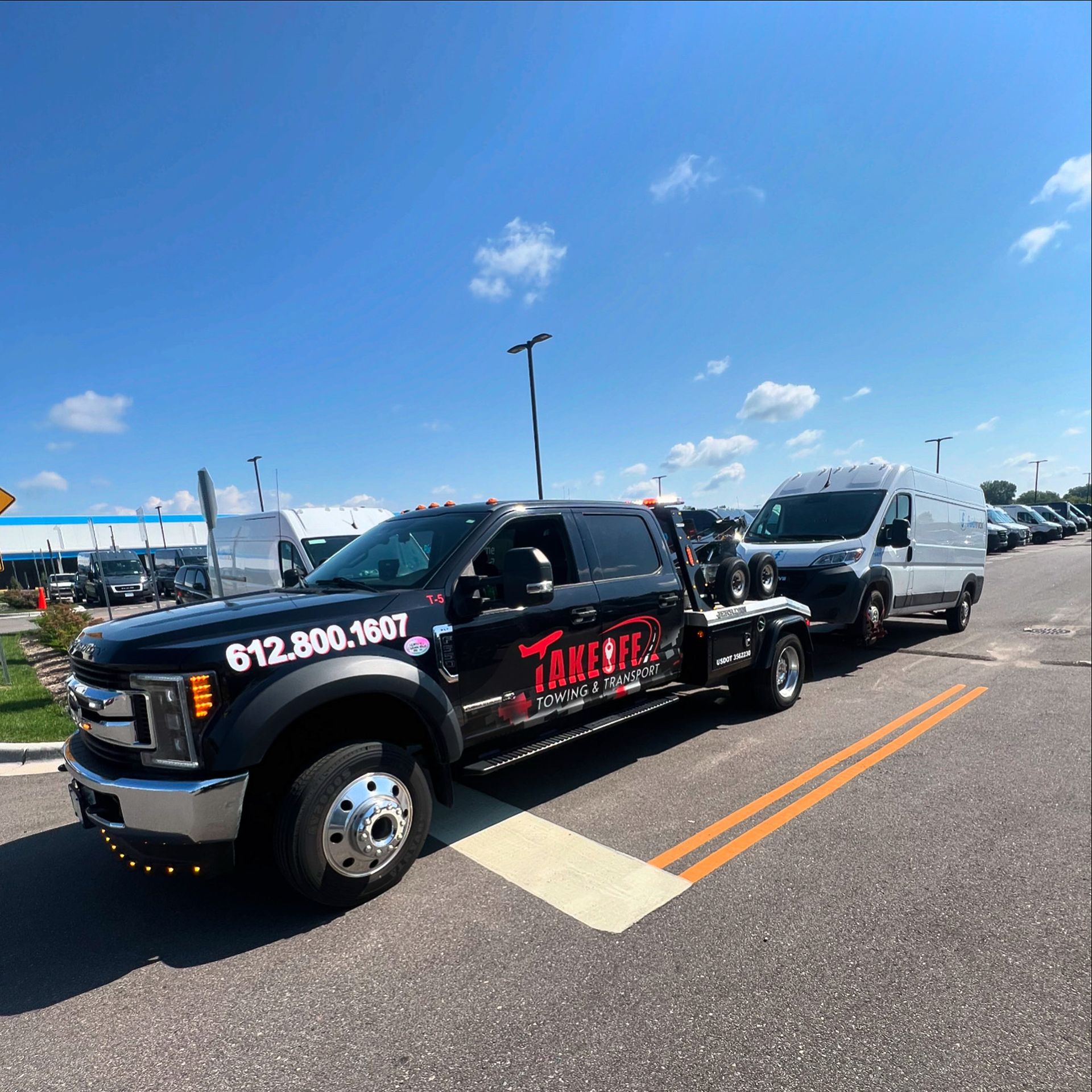 A black tow truck pulling a white van on a sunny day. The truck has red lettering 