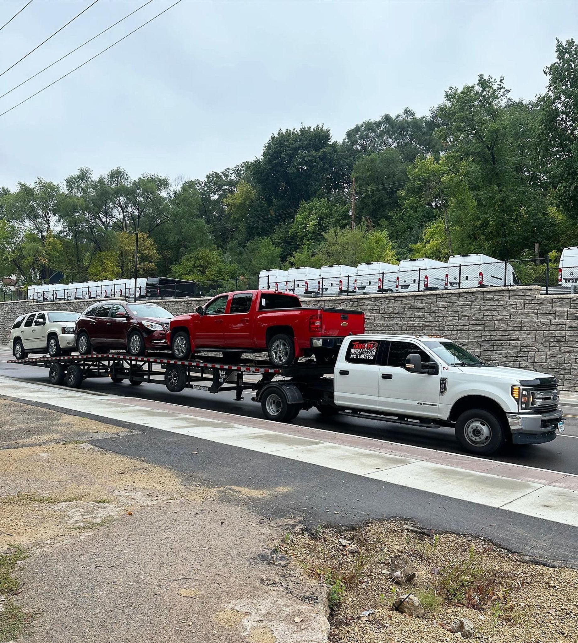 A white truck hauling a trailer with three cars of different colors on a road.