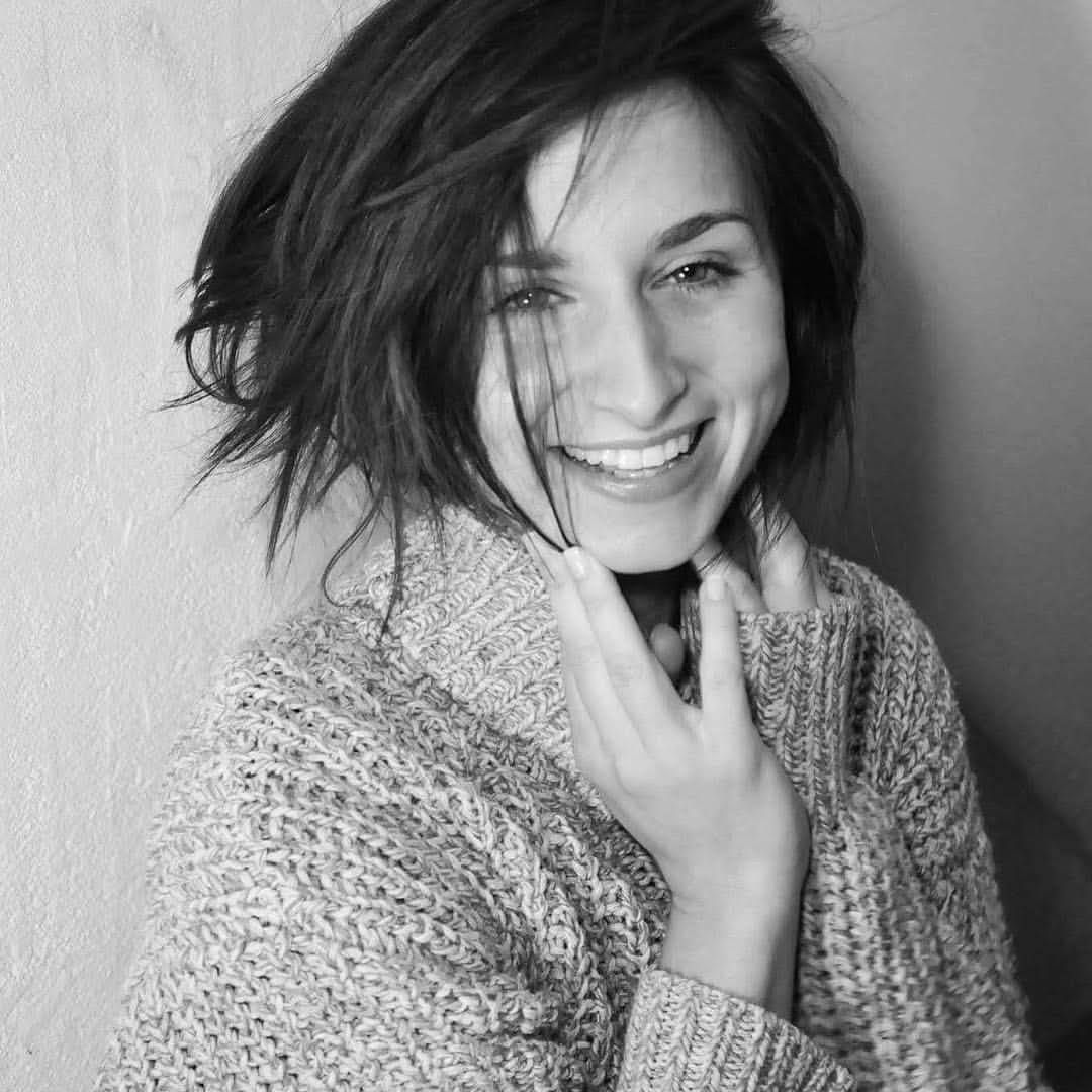 A black and white photo of a woman wearing a sweater and smiling.