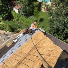 Couvreur sur un toit en pente, posant des bardeaux. Arbres verts et pelouse en arrière-plan.