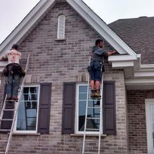 Deux ouvriers sur des échelles installent des gouttières sur une maison en briques.