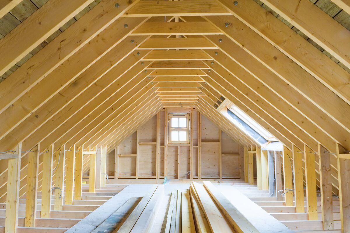 Wooden attic under construction with exposed rafters and window.