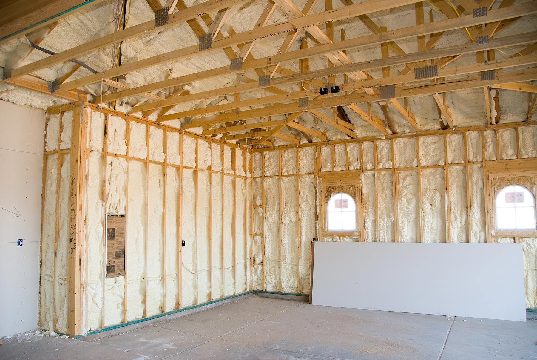 Interior of a building under construction, walls and ceiling insulated with yellow foam, wood frame visible.