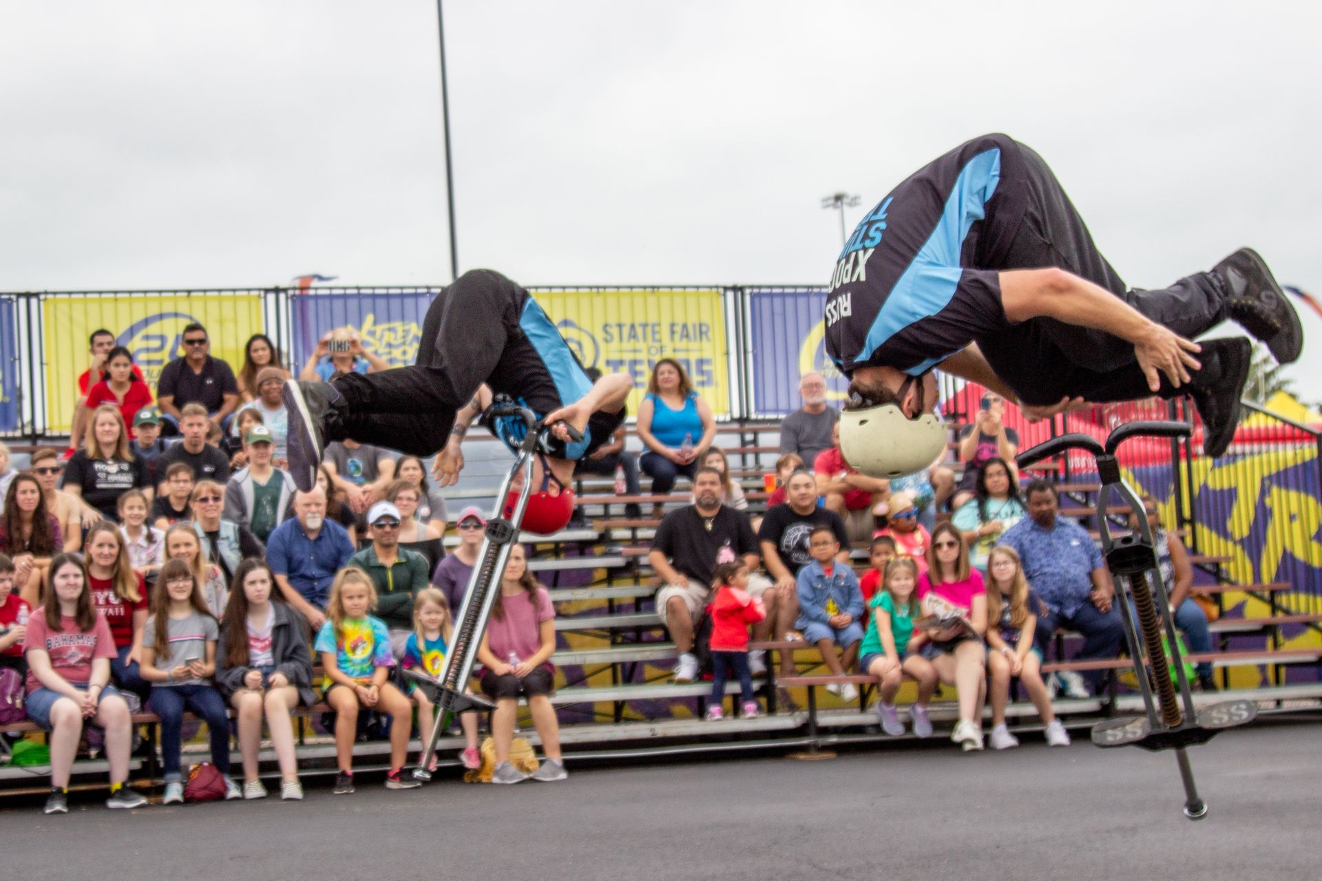 Two men are doing a trick on a bicycle in front of a crowd.