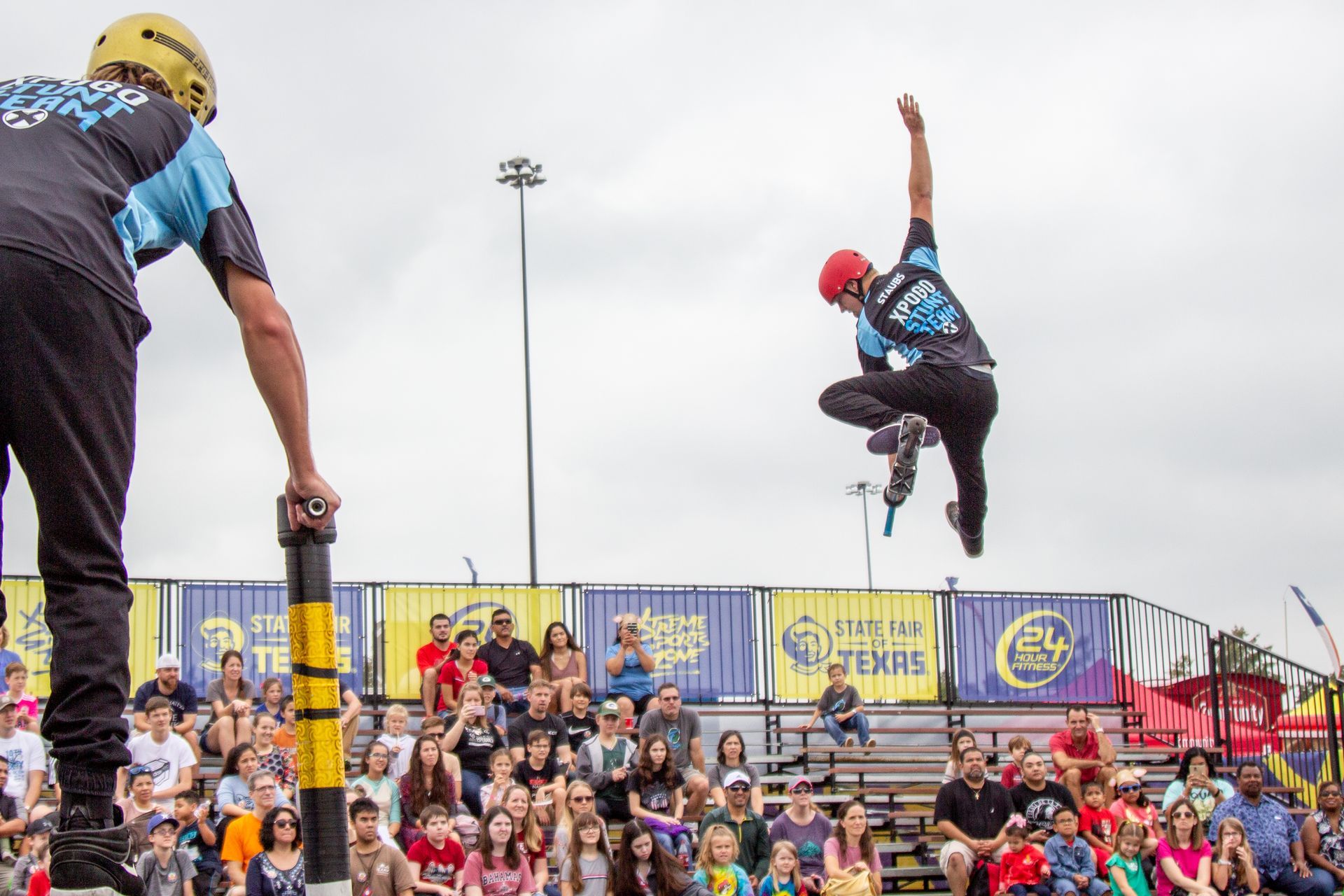 A man is doing a trick on a pole in front of a crowd.