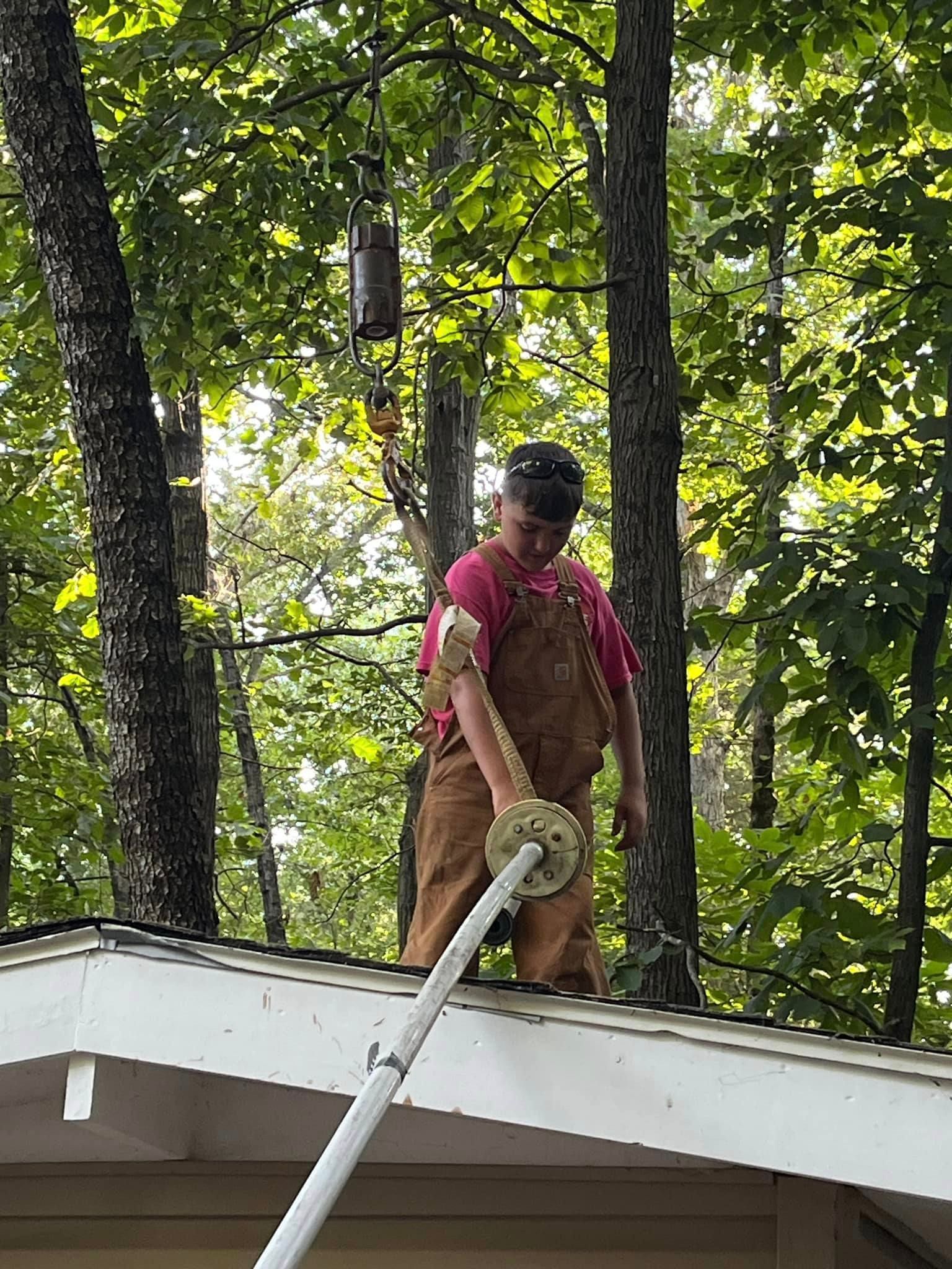 A man is standing on the roof of a house holding a hose.