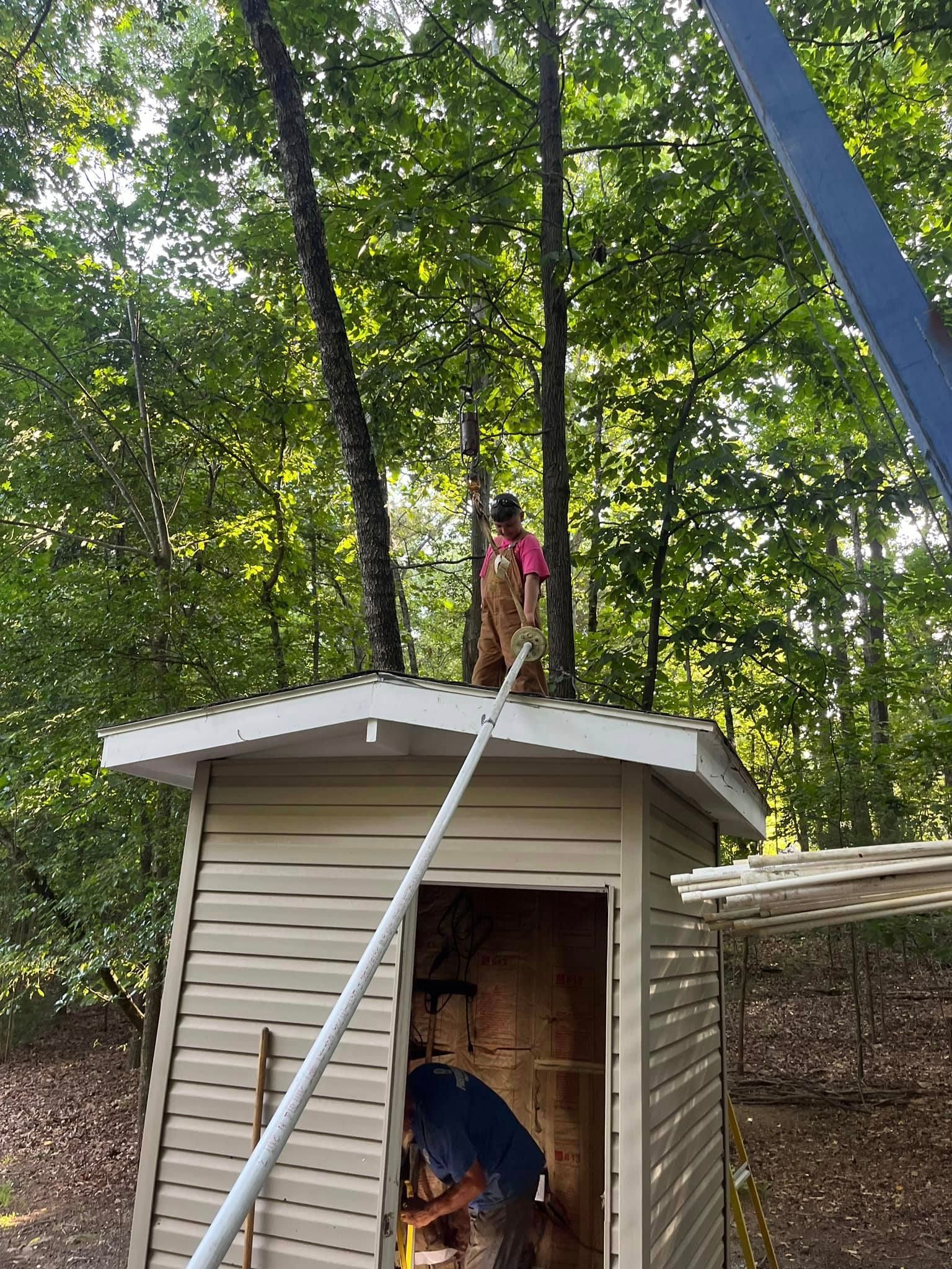A man is working on the roof of a shed in the woods.