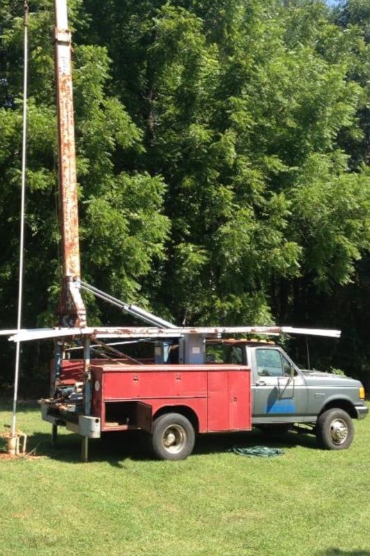A red truck is parked in a grassy field with trees in the background.