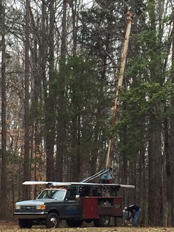 A truck with a crane attached to it is parked in the middle of a forest.