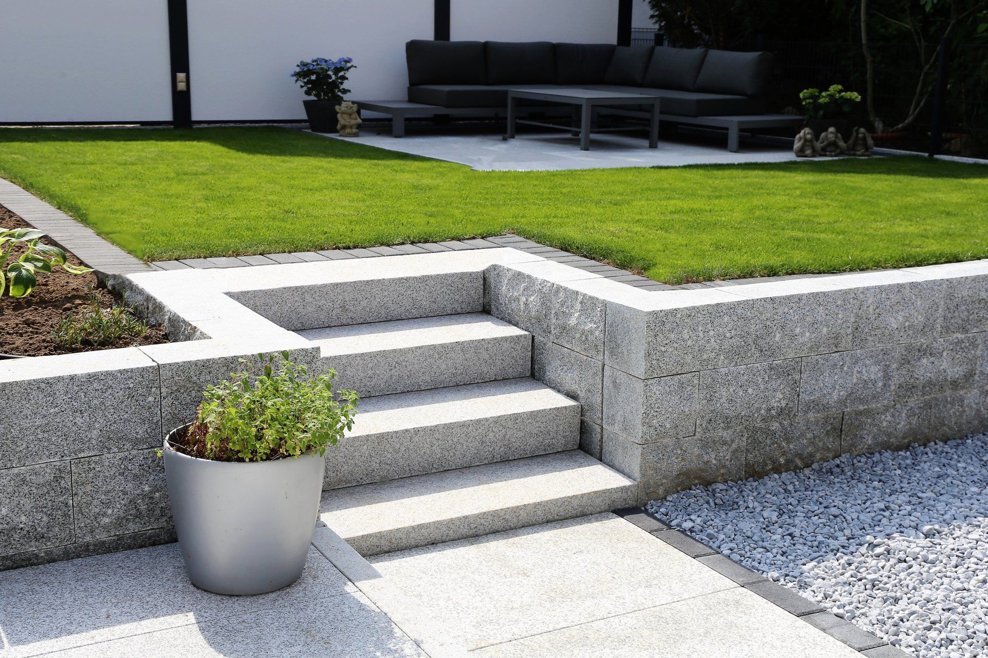 Modern concrete patio steps beside a green lawn, with a potted plant in front and outdoor seating in back